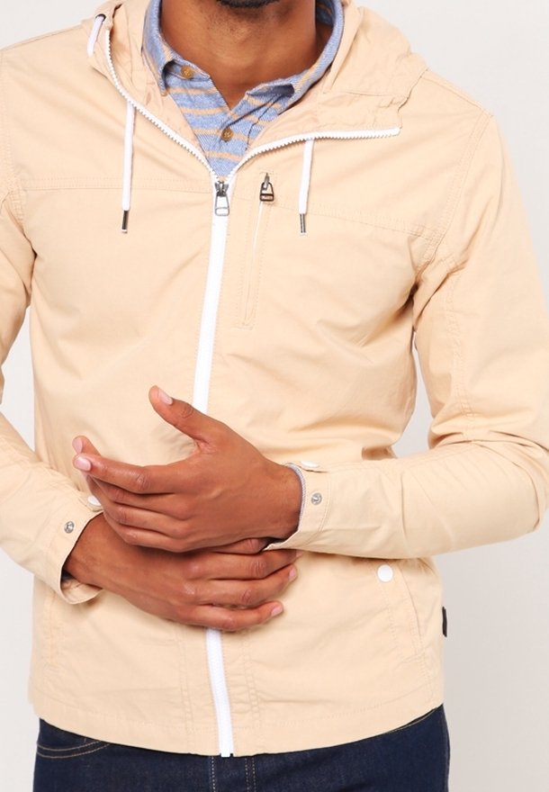 Light beige zip-up jacket with a hood, white zipper, and subtle shoulder seams. Features snaps at cuffs and a front pocket with zipper.
