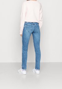 Sytt blå denimjeans med en slät struktur, medelhög midja och två bakfickor. Bärs med en rosa sweatshirt och vita sneakers.