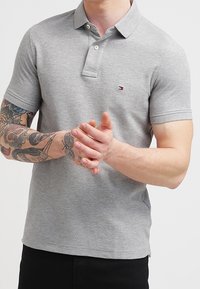 Polo gris en mélange de coton, avec un col, une patte de boutonnage à deux boutons et un petit logo sur la poitrine. Manches courtes et design ajusté.