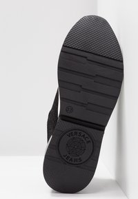 Semelle de chaussure noire avec grip texturé, taille 37, et logo Versace Jeans embossé près du talon.