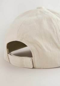 Casquette beige en coton non structuré avec une visière incurvée, des coutures visibles et une sangle réglable à l'arrière. Matériau texturé.