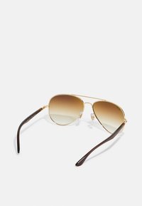 Ochelari de soare aviator din metal aurit, cu lentile gradiente de culoare brună și brațe din plastic brun închis. Pernițe nazale clare pentru confort.