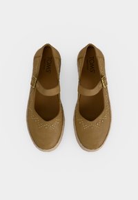 Paire de ballerines Mary Jane couleur beige avec brides à la cheville, clous décoratifs sur la zone des orteils, et semelles intérieures de marque portant l'inscription "TOMS Wear Good."