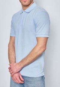 Polo shirt à manches courtes bleu clair avec un col, design ajusté et texture lisse, porté avec un denim bleu clair.