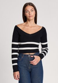 Maglione a strisce bianche e nere con scollo a V profondo, orli a costine e design aderente cropped, abbinato a jeans blu a vita alta.