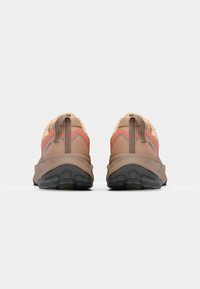 Une paire de chaussures de course beige avec des accents orange, un dessus en tissu texturé, des languettes au talon et une semelle extérieure en caoutchouc noir avec un motif de grip.