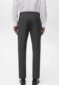 Pantaloni formali grigi con vestibilità su misura, dotati di due tasche posteriori e una piega lungo la gamba; indossati con una camicia bianca a maniche lunghe.