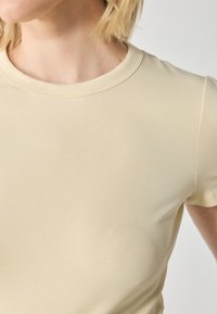 Short-sleeve, crew-neck t-shirt in light beige, made from soft, stretchy cotton material with a smooth texture and minimal stitching details.