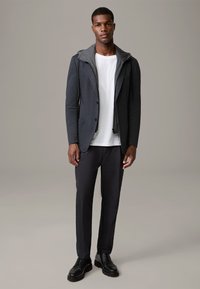 Szary blezer z kapturem, połączony z białym t-shirtem, ciemnymi spodniami i czarnymi butami na sznurówki. Charakteryzuje się swobodnym, przemyślanym krojem.