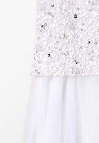 Witte jurk met een versierde bovenkant van glinsterende ronde pailletten en een doorzichtig tule rokje, dat een gelaagde textuur en ontwerp benadrukt.