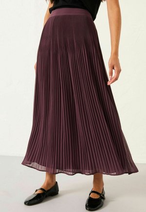 Long, pleated skirt in deep burgundy, featuring a smooth waistband and flowing fabric that extends to mid-calf, paired with black flats.