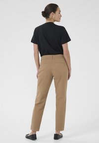 T-shirt noir à manches courtes, pantalon chino beige, design élégant, texture lisse, deux poches arrière, associé à des ballerines noires, vu de dos.