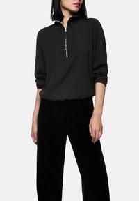 Pull noir zippé avec un col montant et des manches trois-quarts, associé à un pantalon noir à rayures. Texture lisse, coupe décontractée.