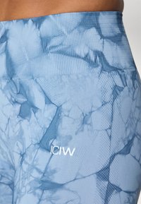 Világoskék leggings, texturált és rugalmas anyagból készült, márványos mintával és fehér nyomott logóval.