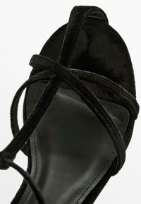 Sandale en velours noir avec des brides croisées, design à bout ouvert, semelle intérieure noire lisse et une semelle matelassée pour le confort.