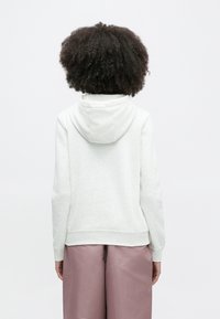 Ανοιχτό γκρι φούτερ με κουκούλα και κορδόνι, υφή χειροτεχνίας και ριμπ μανσέτες. Συνδυάζεται με φαρδιά, ανοιχτό ροζ παντελόνια.