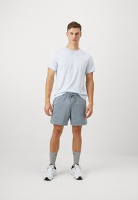 Tricou cu mânecă scurtă de culoare albastră deschisă, pantaloni scurți gri cu șnur, șosete gri și încălțăminte sport albă. O ținută sport simplă și casual.