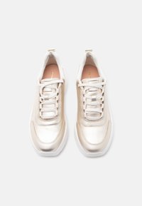 Ζευγάρι μεταλλικά χρυσά αθλητικά παπούτσια με λευκά κορδόνια και σόλες, σε άποψη από πάνω, σε απλό λευκό φόντο.