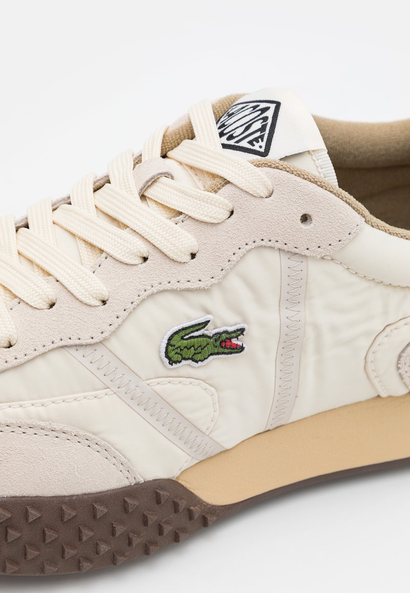 Baskets beiges avec un dessus en cuir texturé et en tissu, présentant un logo crocodile brodé vert et une semelle en caoutchouc marron.