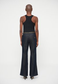 Débardeur noir et pantalon en denim foncé à jambe évasée. Le pantalon présente un accent chaîne au niveau de la taille et a une finition lisse et texturée.