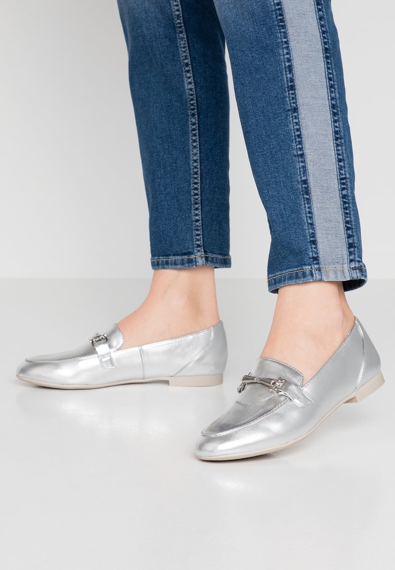Chaussures plates argentées à finition métallique lisse, ornées d'une petite lanière décorative et d'un design à bout arrondi.