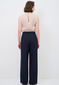 Beige ärmlös topp med detalj i ryggen i form av nyckelhål, tillsammans med vida marinblå byxor som har sidoficka och en slät yta.