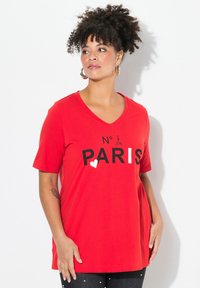 Červené tričko s výstřihem do V vyrobené z bavlny, na kterém je černý nápis "N° PARIS" a grafika srdce, s krátkými rukávy a volným střihem.