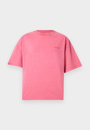 Camiseta rosa de gran tamaño con mangas cortas y cuello redondo, con un pequeño logo sutil en el pecho izquierdo, presentada sobre un fondo claro y sencillo.