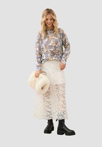 Bloemige trui in blauw, geel en paars; witte kanten maxi-jurk; zwarte chunky laarzen; houdt een crèmekleurige nepbont tas vast.