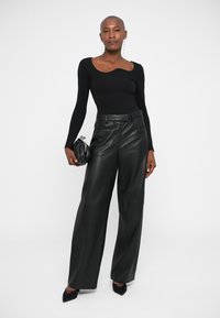 Top negro de manga larga con escote en forma de u, combinado con pantalones de cuero de pierna ancha de cintura alta y un pequeño bolso de mano negro. Tacones negros clásicos.