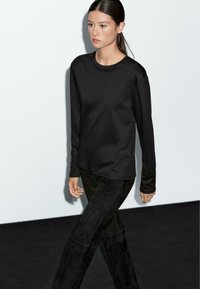 Zwarte lange mouwen top met een ronde halslijn, gecombineerd met donkere, gestructureerde broek. Eenvoudig ontwerp, gladde stof en slim fit. Minimalistische stijl.