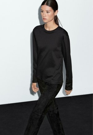 Black long-sleeve top with a round neckline, paired with dark, textured pants. Simple design, smooth fabric, and slim fit. Minimalist style.