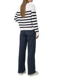 Wit en marineblauw gestreepte trui met lange mouwen; samen met donkere blauwe wijde jeans en witte sneakers. Ontspannen pasvorm en ribgebreide manchetten.