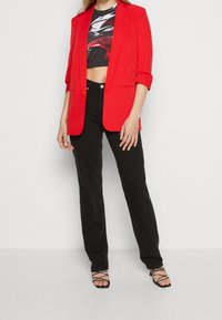 Röd skräddarsydd blazer med en strukturerad design, i kombination med en svart crop top, svarta raka byxor och svarta sandaletter med klack och remmar.