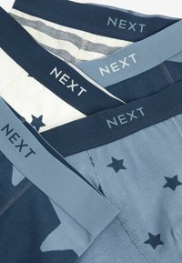 Tre par boxershorts i olika nyanser av blått och vitt. Funktioner inkluderar elastiska band med "NEXT"-logotyp och stjärnmönster.