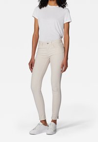 Jean skinny beige clair à taille mi-haute, fabriqué en denim, assorti à un t-shirt blanc simple et des baskets blanches. Texture lisse, coupe ajustée.