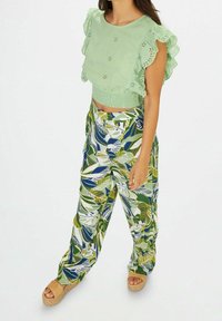 Top court brodé vert clair avec des manches volantées, associé à un pantalon large avec un motif de feuilles coloré. Sandales à plateforme beige.