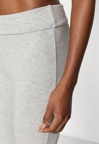 Κολάν με γκρι ελαστική μέση κατασκευασμένο από απαλό, υφασμένο ύφασμα. Κοντινό πλάνο της μέσης και του χεριού τοποθετημένου κοντά στη ραφή στο πλάι.