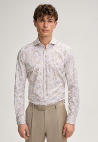 Weißes Langarmhemd mit einem floralen Muster in Beige und Hellbraun, mit Button-Down-Kragen und figurbetontem Design. Kombiniert mit beigen Hosen.