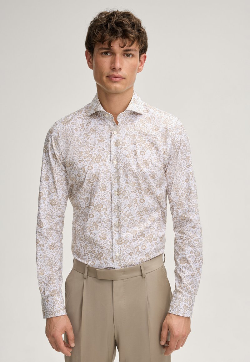 Weißes Langarmhemd mit einem floralen Muster in Beige und Hellbraun, mit Button-Down-Kragen und figurbetontem Design. Kombiniert mit beigen Hosen.
