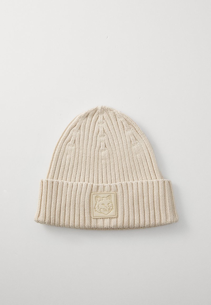 Beige knit beanie with ribbed texture, folded cuff, and a square patch featuring a fox design in subtle relief. Soft, warm material.
