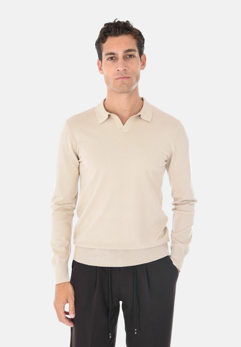 Maglione polo maniche lunghe beige con colletto a V e orlo a coste. Tessuto morbido con un design aderente, abbinato a pantaloni neri.
