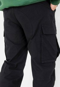 Zwarte cargobroek met zijzakken, een gebogen naad op de achterkant en een textuurstof. Ontworpen voor functionaliteit en comfort.