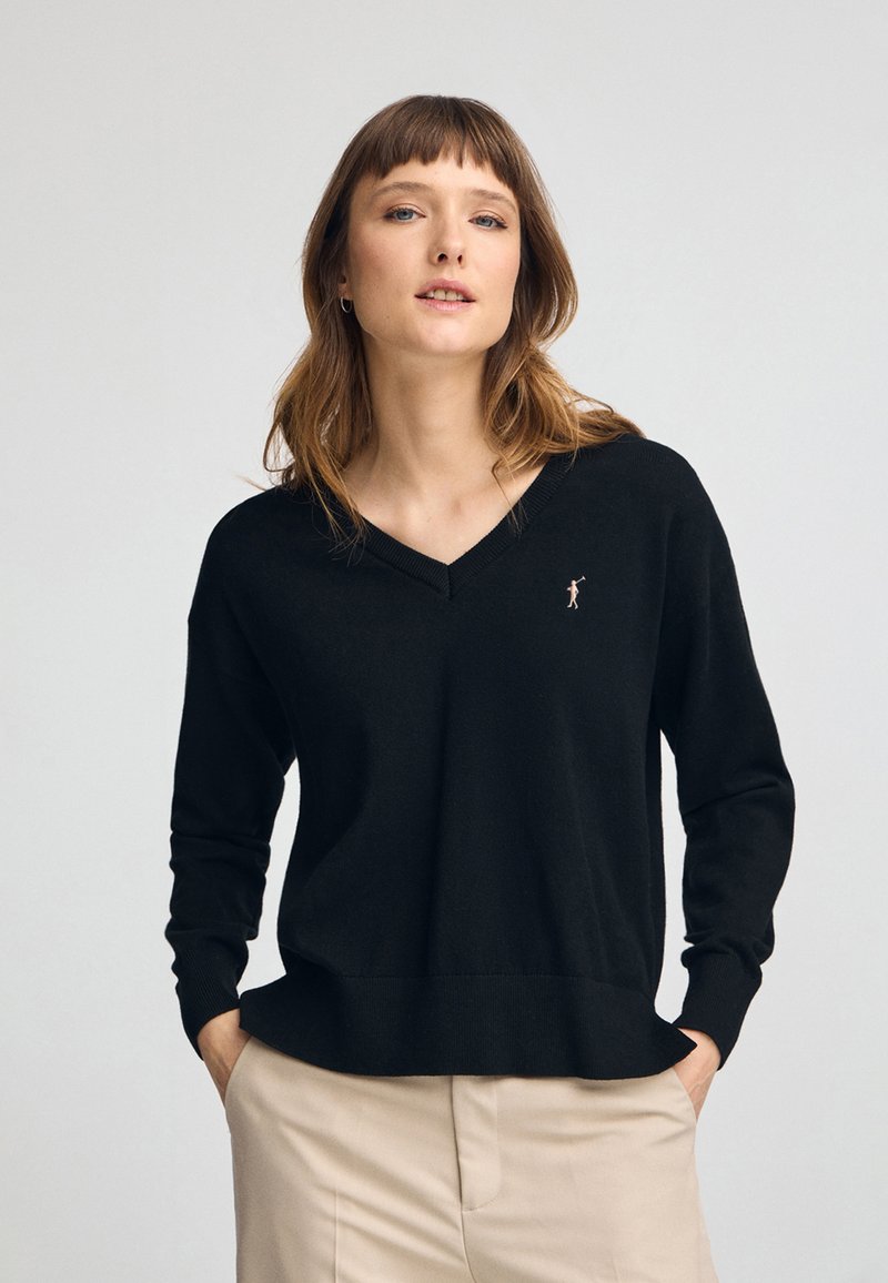 Pull noir en maille avec un décolleté en V et des poignets côtelés. Présente un petit motif brodé sur la poitrine. Texture douce, coupe décontractée.