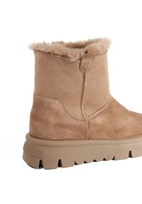 Tan suede ankle boots with a soft shearling lining, round toe, side zipper, and a thick, textured rubber sole featuring scalloped edges.