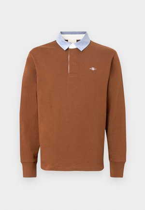 Brun långärmad pikétröja med ljusblå krage, med en liten logotyp på bröstet och ribbade muddar, tillverkad av mjukt tyg.