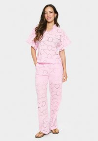 Completo a due pezzi di un delicato rosa chiaro, realizzato in tessuto ricamato con motivi a taglio. Presenta una maglietta a maniche corte e pantaloni a vestibilità comoda.