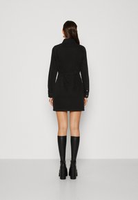 Černé džínové košilové šaty s dlouhými rukávy a límečkem, se zvýrazněným pasem a krátkou délkou. V kombinaci s černými vysokými kozačkami.