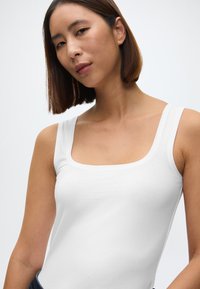 Biała bezrękawnik z miękkiego materiału, z kwadratowym dekoltem i szerokimi ramiączkami, o gładkiej fakturze i dopasowanym kroju.
