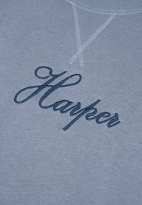 Felpa azzurra chiara con ricamo corsivo blu scuro del nome "Harper". Il materiale sembra morbido e texturizzato con il design a collo rotondo.
